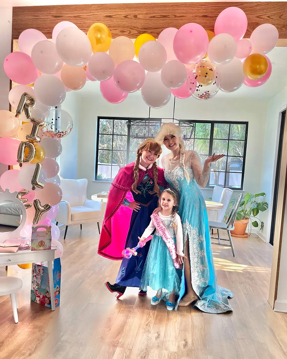 anna and elsa party with a little girl under balloon arch